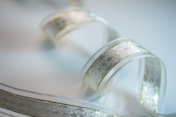 Full frame macro defocused background of silvery white brocade fabric ribbon with golden accent stitches on white background, with copy space