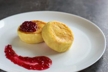 Cottage cheese pancakes or syrniki with raspberry jam on white plate on dark background, healthy breakfast. Concept of Russian and Ukrainian cuisine.