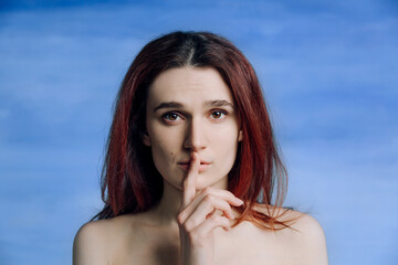 A young girl, with bare shoulders pressed her finger to his lips in gesture silently and looks to the side A person expresses anxiety.