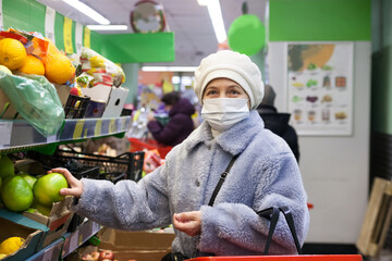 Fototapeta na wymiar Woman in protective mask with shopping cart in grocery hypermarket