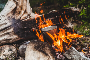 Kettle hanging over fire. Cooking food at fire in wild. Beautiful big log burns in bonfire close-up. Survival in wild nature. Wonderful flame with caldron. Pot hangs in flames. Campfire background.