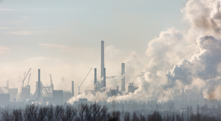 Smoke from chimneys at the plant in the rays of the sunset as a background.