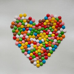 Heart of multicolored round candies on a gray background.