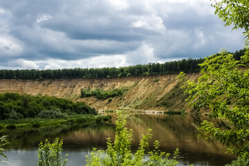 A wide river flows into the distance next to a steep sandy shore.  Trees grow along the banks.  Summer, beautiful landscape