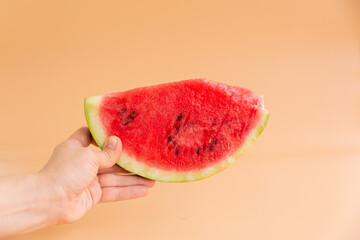 A female hand holds a slice of watermelon on an orange background