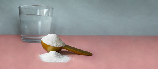 Gold measuring spoon with collagen and glass of water on pastel pink gray background. Horizontal banner for website or social networks with space for text. Powdered hydrolyzed fish collagen supplement