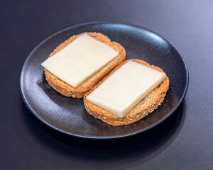 whole grain and sesame rusks with low fat cheese in black dish on black table