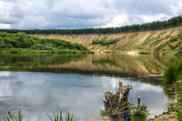 A wide river flows into the distance next to a steep sandy shore.  Trees grow along the banks.  Summer, beautiful landscape