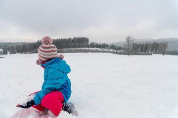 Fototapeta na wymiar Kind im Skianzug und dicke Mütze spielt im Schnee.