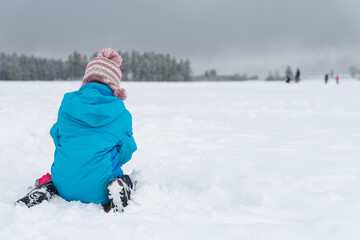 Fototapeta na wymiar Kind sitzend spielt mit Schnee, Rückenansicht