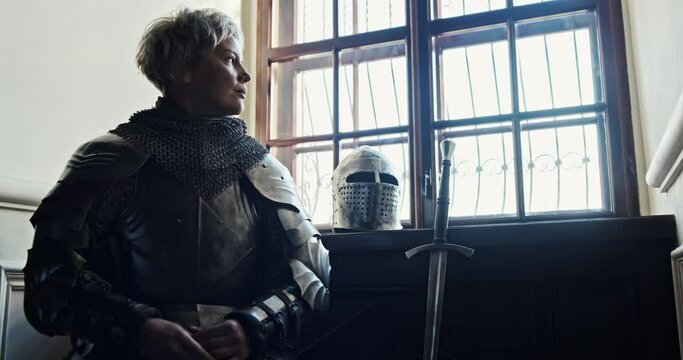 Medieval period a woman warrior bravely sits in a castle near his sword and helmet in knightly iron armor