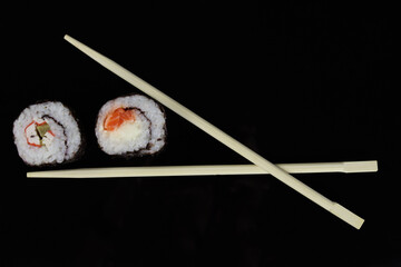 chopstick holding a sushi roll on a black background