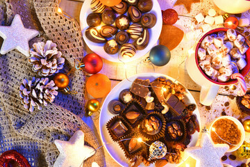 sweet food top view background for merry christmas or new year holiday decoration with night illumination - chocolate candies, tangerines, cookies, marshmallow and cocoa latte on white wood