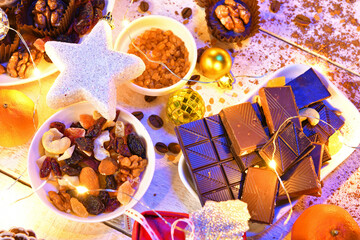 sweet food top view background for merry christmas or new year holiday decoration with night illumination - chocolate candies, tangerines, cookies, marshmallow and cocoa latte on white wood