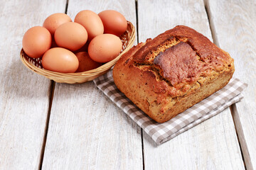 Loaf of bread and basket of eggs on white wooden table.