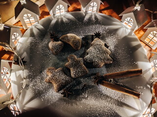 Homemade cookies in the shape of a heart and christmas tree in a white plate and and a garland in the form of houses. Cozy Christmas evening with homemade cookies . Selective focus.