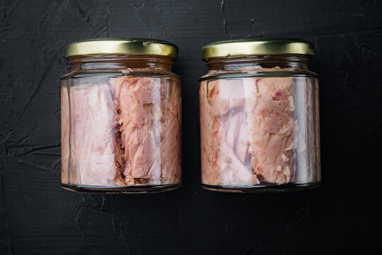 Tuna fillet in glass jar, on black background, flat lay