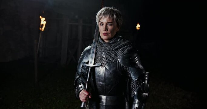 History of the Middle Ages independent strong free woman warrior standing in knightly armor and with a sword in his hands on a background of burning torches