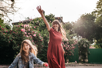 mother with emotional and active daughter walk in the park and scatter flower leaves