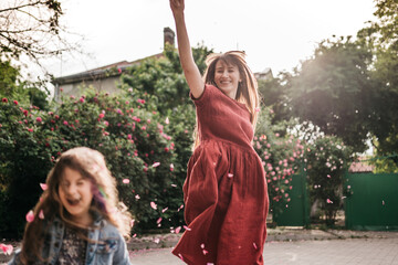 happy mother with emotional and active daughter walk in the park and scatter flower leaves