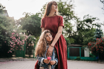 happy mother in red dress hugs her beautiful preschool daughter in spring park with roses
