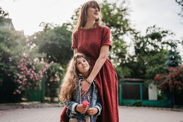 mother in red dress hugs her beautiful preschool daughter in spring park with roses