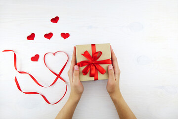 Women's hands hold a gift box. Valentines Day, Birthday. Ribbon heart, romantic decoration on white wooden background.