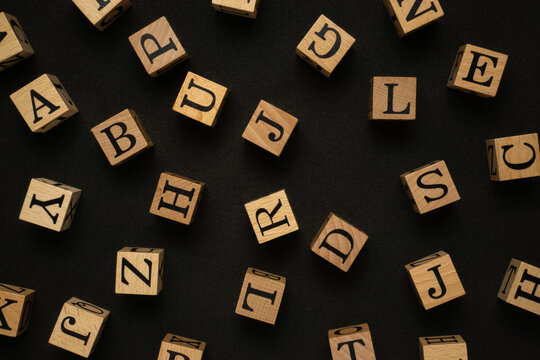 Uppercase alphabets on a wooden cube with a black background.