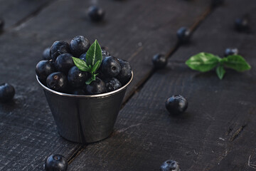 Freshly picked blueberries in wooden bowl. Juicy and fresh blueberries with green leaves on rustic table. Bilberry on wooden Background.