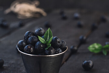 Freshly picked blueberries in wooden bowl. Juicy and fresh blueberries with green leaves on rustic table. Bilberry on wooden Background.