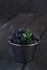 Freshly picked blueberries in wooden bowl. Juicy and fresh blueberries with green leaves on rustic table. Bilberry on wooden Background.