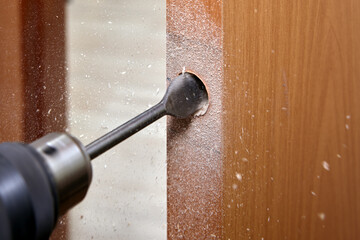 The carpenter uses a flat bit shank drill for wood to drilling a handle hole with a lock for an...