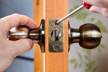 Installation of new brass door handles with a latch in a wooden interior door, a locksmith's hand...