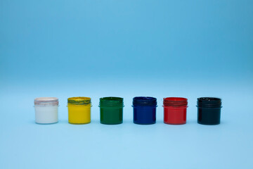 Plastic jars with multicolored paints on a blue background. Several colours of gouache, acrylic...