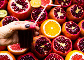 The glass of pomegranate juice in the woman hand on the fruit natural background.
