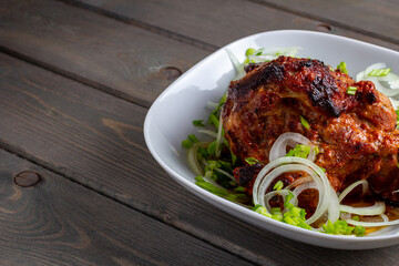 Side view of a piece of baked juicy pork with green onions on a white plate on a wooden background.
