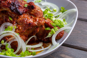 close-up of baked pork neck meat with green onions and rings on a white plate on a wooden background.