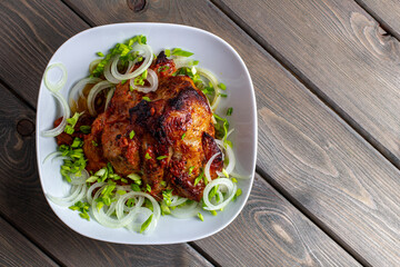 Top view of baked pork neck meat with green onions and rings on a white plate on a wooden background.
