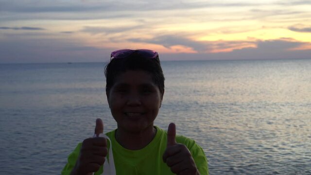 Smart Asian woman take facemask out of danger be secure when relaxing on sunset beach, Smiling woman in disposable protective surgical mask period of coronavirus covid-19 pandemic on seabeach