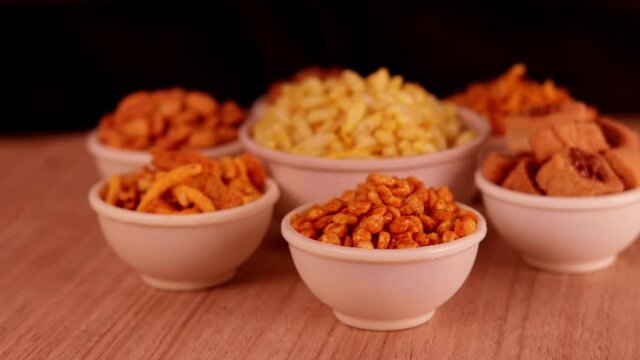 black background with Namkeen or Assorted Salty Snack on wooden spoon in white bowl close up, indian sneak,Namkeen in a bowl,Namkeen or Assorted Salty Snack on wooden spoon in white bowl,Namkeen,