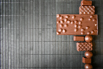 Various types of chocolate sweets with nuts, waffles in a row on the table with place for text