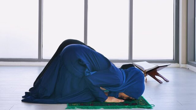 Two Asian Muslim young women in traditional hijab are praying glorify Allah and practicing the Islamic faith in mosque.