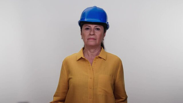 An old female civil engineer wearing a blue hard hat.Elderly engineer woman in blue hard hat smiling at the camera on a white background.