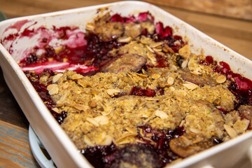 A baking trey of delicious plum and blackberry crumble on a wooden kitchen work top.