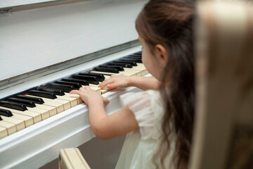 Little girl plays on a white piano.