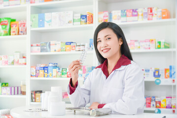 Beautiful asian professional young pharmacists holding medicine and standing with smile at drugstore.