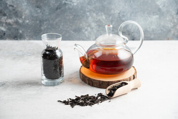 A glass teapot with dried loose teas and a wooden spoon