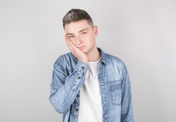 Studio shot of an annoyed annoyed handsome guy who touches his face and bends over, looks out from...