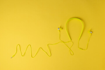 Yellow sports headphones with a wire on a yellow background.