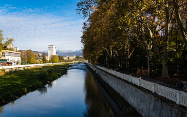 Obraz premium Sochi, Russia - November 23, 2020: Hotels on Sochi river embankment. City center. Golden autumn. Beautiful view of Sochi River, embankment with trees and snow-capped peaks of Main Caucasian ridge.